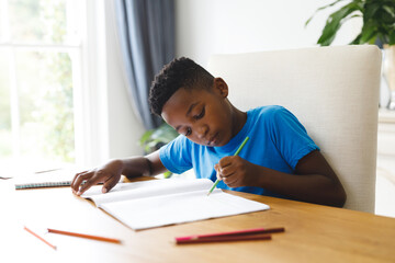 African american boy sitting at table in living room, doing homework