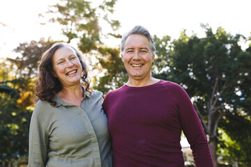 Obraz premium Portrait of happy senior caucasian couple embracing, looking to camera in sunny garden