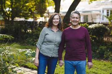 Portrait of happy senior caucasian couple holding hands, looking to camera in garden