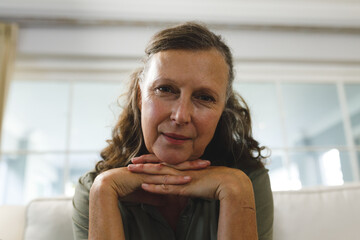 Smiling senior caucasian woman in living room, sitting on sofa, making video call