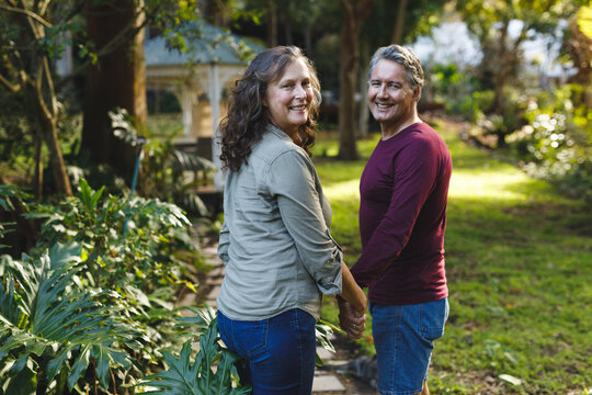 Portrait of happy senior caucasian couple holding hands, looking to camera in sunny garden