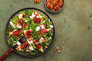 Fig salad with white cheese, walnuts, arugula and jam dressing on rust green background, top view, copy space