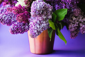 bouquet of lilac flowers in golden zinc pot on a lilac background