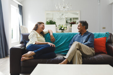 Happy senior caucasian couple in living room sitting on sofa, talking