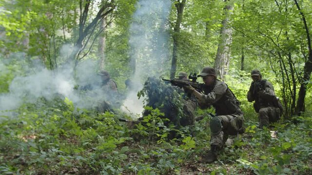 Military counter-terrorist group in camouflage setting fire to smoke grenades, throwing bombs ahead, getting ready to attack enemy position in forest area during danger reconnaissance mission