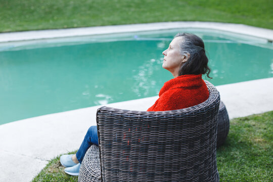 Thoughtful Senior Caucasian Woman Sitting On Chair By Pool In Garden