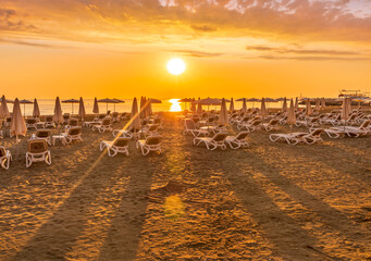 Obraz premium tranqiul sunrise an a beautiful beach with umbrellas on thr foreground , golden sand and sun rays and calm sea on the background