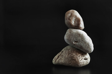 Three stones stand on top of each other keeping their balance. Dark background. Copy space..