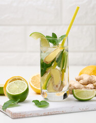 Fototapeta premium transparent glass cup with lemon, lime pieces and mint leaves and ginger pieces on a white table, detox.