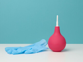 pink rubber enema on white table, medical instrument for cleaning the body, blue background