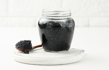 fresh black paddlefish caviar in a wooden brown spoon and a full can of caviar on a wooden white table