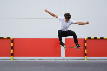 young skater does tricks outdoor. background is white and red wall - obrazy, fototapety, plakaty