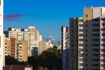 Fototapeta na wymiar Kyiv, Ukraine. July 8, 2021. Multistory buildings against a blue sky at sunny day. A city street stretching into a distance buried in green trees. Walls and windows of high post soviet union buildings