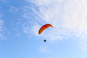 Orange paraglider is flying in the blue sky against the background of clouds. Paragliding in the...