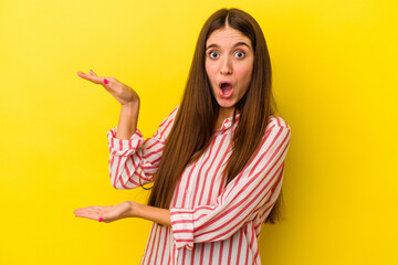 Young caucasian woman isolated on yellow background shocked and amazed holding a copy space between hands.