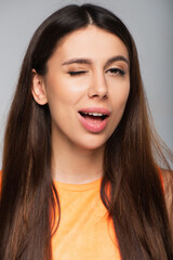 Naklejka premium flirty young woman winking eye isolated on grey