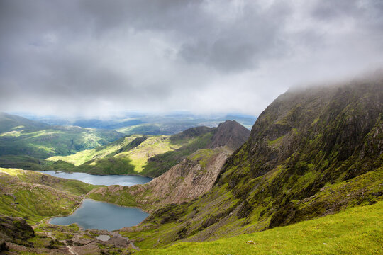 A panoramic view of the mountains and lakes of Snowdonia, North Wales. Summer day with low clouds and the lush green grass of the Welsh countryside.