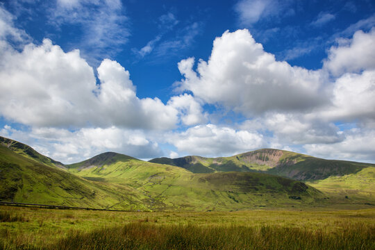 A panoramic view of the mountains of Snowdonia, North Wales. Summer day with blue sky and puffy clouds and the lush green grass of the Welsh countryside.
