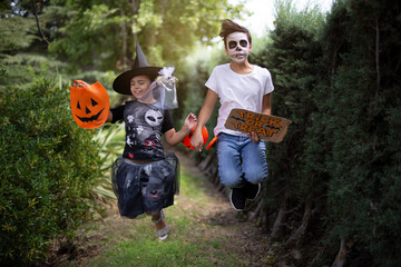 Caucasian boy and girl in typical Halloween costumes jumping and having fun outdoors. 