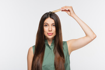 young woman massaging hair with metallic massage tool isolated on grey