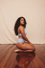 Young woman kneeling while wearing blue underwear in a studio - obrazy, fototapety, plakaty