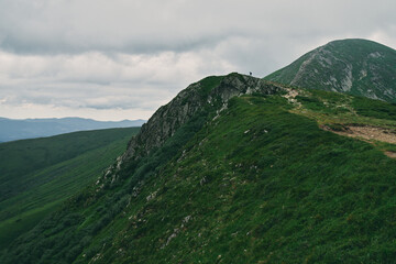 A landscape of a mountainous area covered with grass and stones. In the distance, a tourist who conquered the top of the mountain. Cloudy mountain landscape.