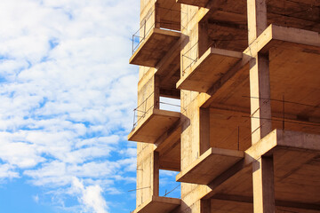 Naklejka premium Concrete construction of a new high-rise apartment building against blue sky. An unfinished buildings facade view from outside. Residential complex exterior. Real estate. Slabs, walls. Copy space.