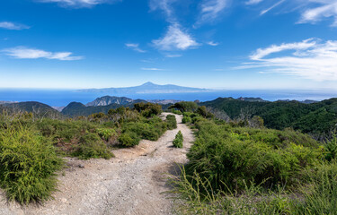 La Gomera - Wanderweg vom höchsten Berg Alto de Garajonay nach Norden mit Blick zur Insel Teneriffa mit Teide  - obrazy, fototapety, plakaty