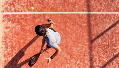 Top view of a paddle tennis player who is hitting the ball on an outdoor court.