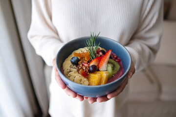 A woman holding healthy blueberry smoothie bowl with mixed fruits topping