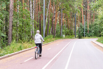Active senior caucasian woman with gray hair is riding bike on bicycle path in forest park.