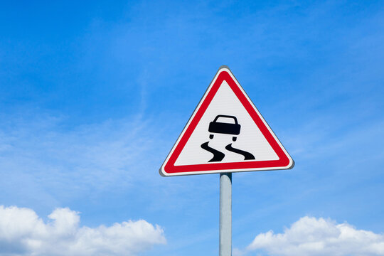 International road sign 'Slippery road ahead' against blue sky