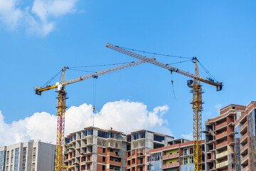 Tower cranes on the background of a house under construction. Blue sky on background