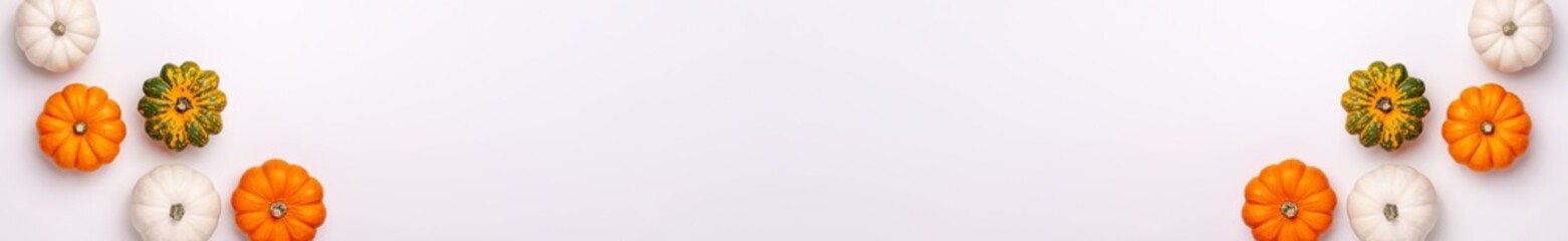 Flat lay banner of mini decorative pumpkin white, orange, yellow and green colors on bright background on the left and right from above at the top. Halloween and Thanksgiving greeting card holiday