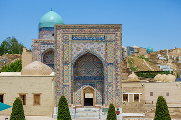 Fototapeta na wymiar Facade view of historical complex Shahi Zinda in Samarkand, Uzbekistan. Behind entrance portal, buildings of mausoleums are visible rising up hill. Some elements of building contain lines from Koran