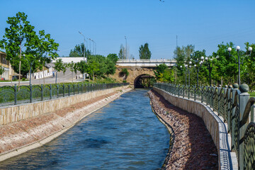 Naklejka premium Siab River flowing through the city of Samarkand, Uzbekistan. Old bridge is visible in the distance, a park on the right