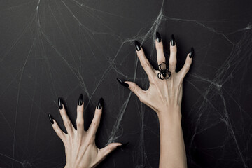 Hands with long black nails and spider ring on a black background with cobwebs. Happy Halloween...