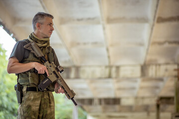 A man standing with an airsoft assault rifle in military uniform in concrete hangar