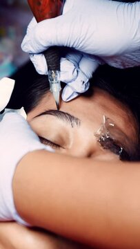 Vertical footage. Close up microblading eyebrow tattoo. Beautician in gloves makes permanent makeup correction of the shape of the eyebrows to a young women. Eyebrow tattoo in a beauty salon.