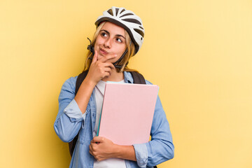 Young caucasian student woman wearing a bike helmet isolated on yellow background  looking sideways with doubtful and skeptical expression.
