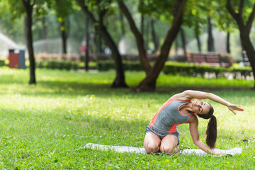 flexible woman in sportswear stretching on yoga mat in park