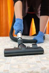 Hands with blue gloves cleaning soft surface with vacuum cleaner. Selective focus