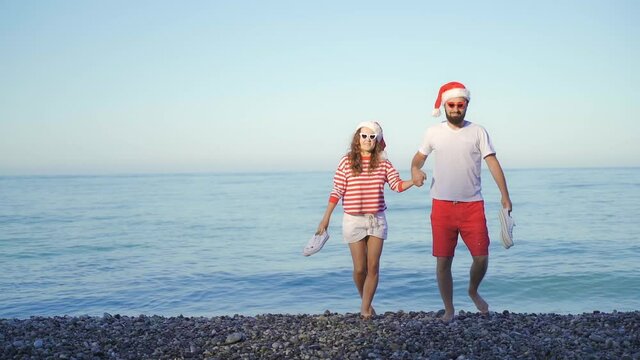Happy woman and man in red Santa Claus hat by the sea. funny girl and a guy with glasses for Christmas. Concept of a family New Year holiday in a warm country on the beach
