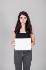 Young girl holding a blank sheet of paper in her hands, isolated on gray background