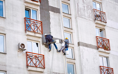  Industrial alpinists at height on rope, plastering wall with trowel. Industrial climber repairing...