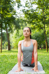 young woman with closed eyes meditating on yoga mat in park