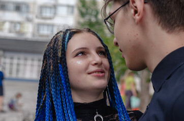A young heterosexual couple looks lovingly into each other's eyes. Young woman with blue pigtails. A young man with glasses. Love, relationships. City street. Selective focus.