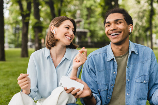 Mixed-race Students Friends Romantic Couple Freelancers Listening To The Podcast Radio Music Favorite Singer Song Playlist In Earbuds Earphones Using Musical Application Walking In City Park Outdoors