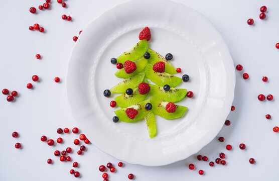 christmas food for kids. white dish with christmas tree made of kiwi, raspberries, cowberry and huckleberry