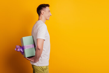 Profile portrait of cheerful nice guy hold persent package behind back make surprise on yellow...